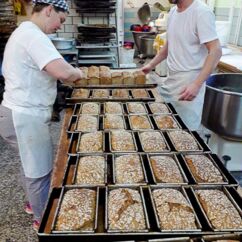 Zwei Bäcker in der Biobäckerei Vogel legen frisch gebackene Brote auf ein Blech