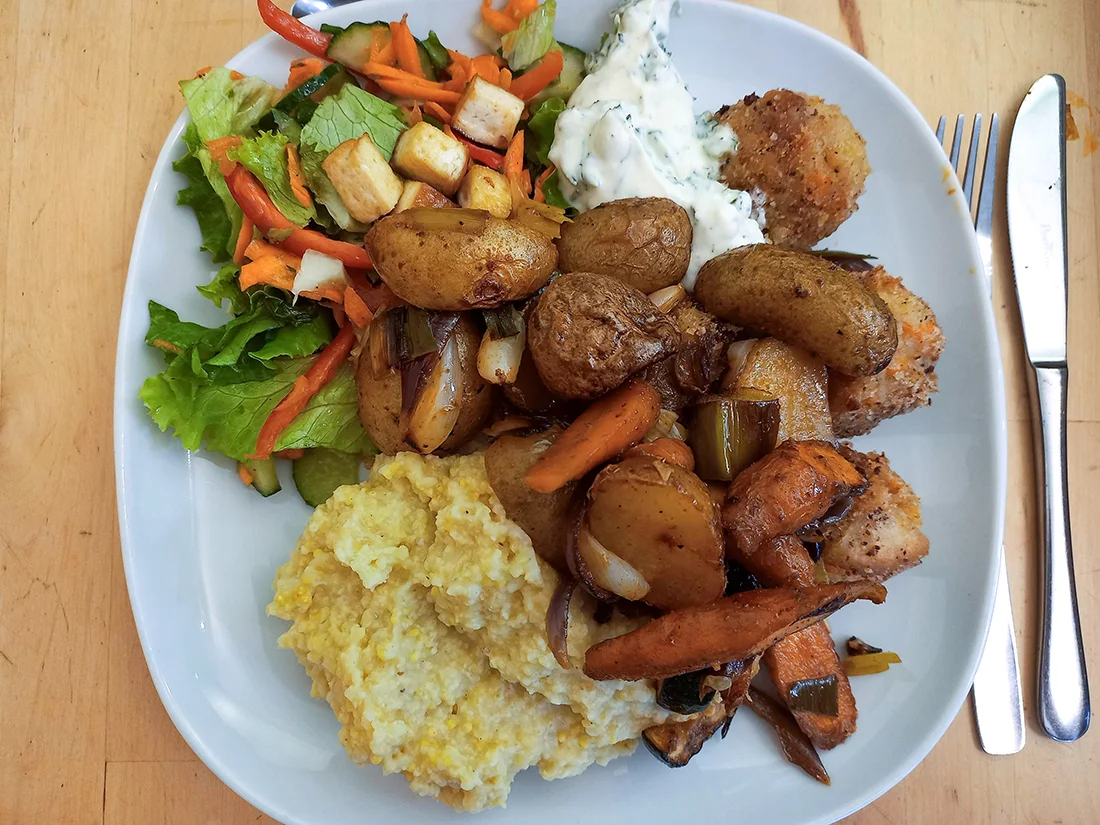 Ein Teller mit Hirsepüree, Salat und gebratenem Gemüse mit Kartoffeln und Pilzen