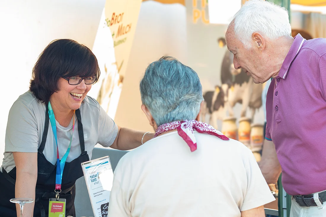 Eine Frau mit zwei Besucherinnen des Regionalfest steht an einem Stand