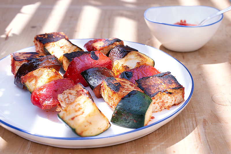 drei Grill-Spieße mit mediterranem Gemüse und mariniertem Tofu, daneben Tomaten-Dip in einer Schale