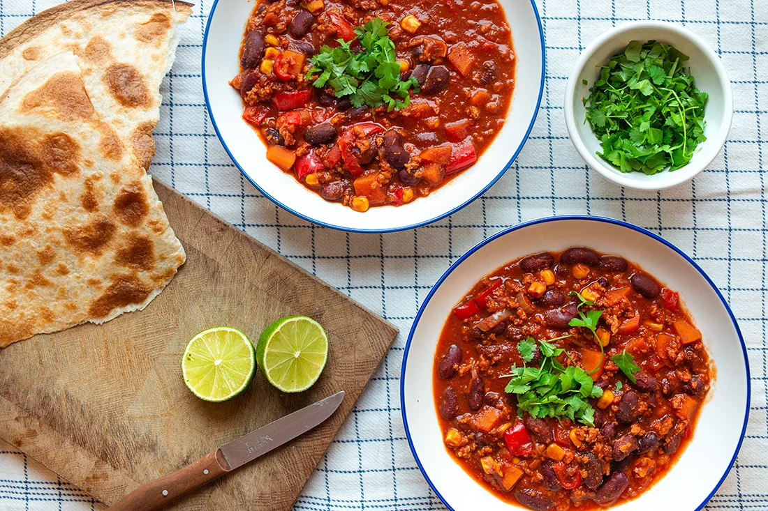 Veganes Chili sin Carne auf Tellern, Limette und Brot auf einem Brett