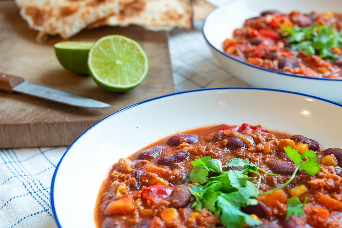 Veganes Chili sin Carne auf Tellern, Limette und Brot auf einem Brett